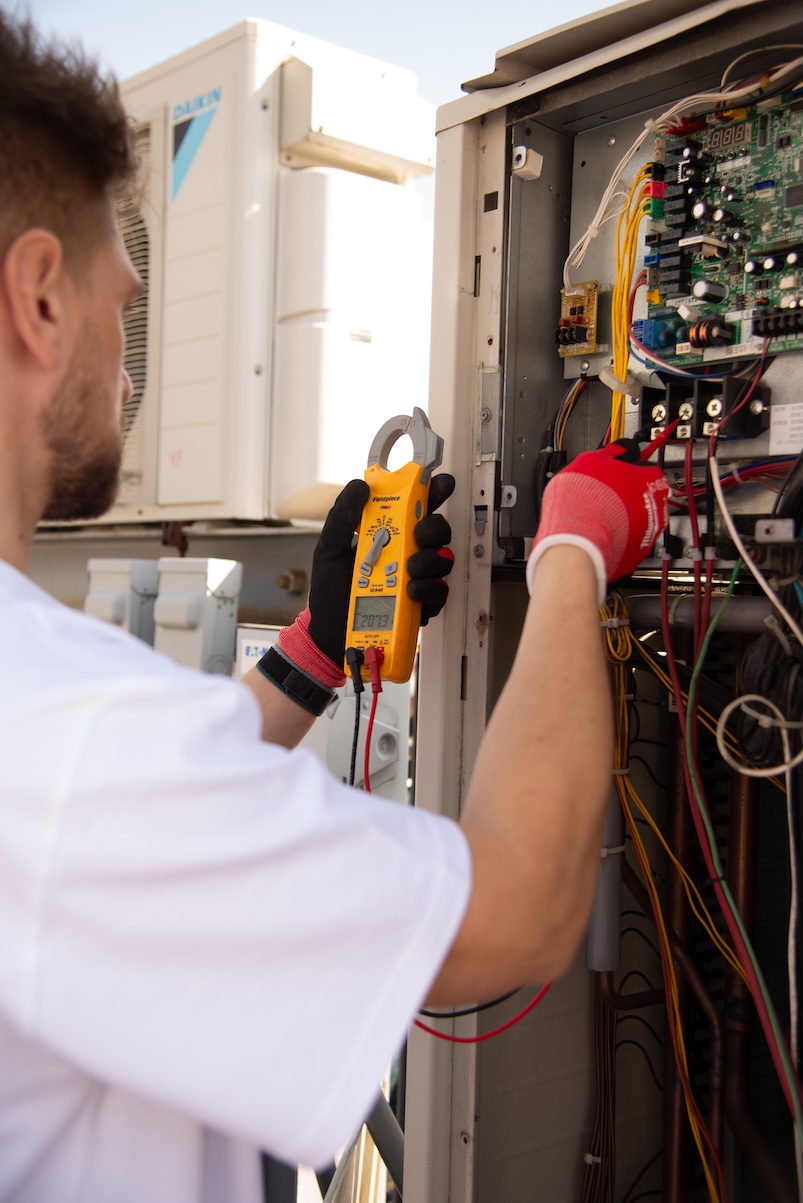 Technician testing electrical on a Daikin outdoor unit